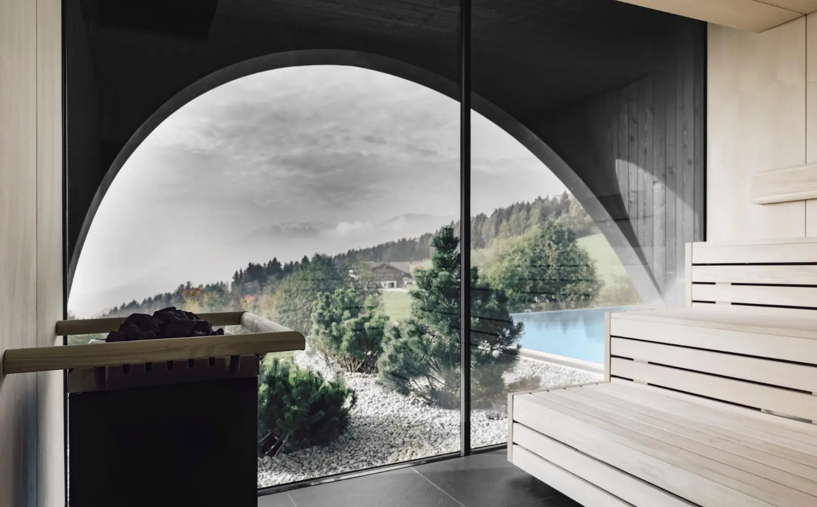 Sauna mit Rundbogen-Panoramafenster und Blick auf Pool und Berglandschaft